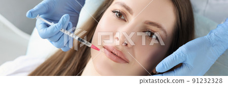 Young woman gets injection of botox in her lips, cosmetologist using syringe 91232328