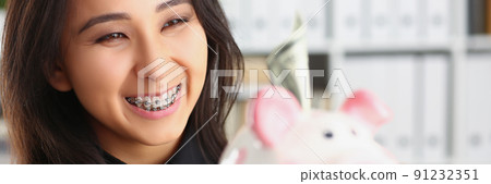 Pretty laughing young woman holding piggybank with banknote in it 91232351