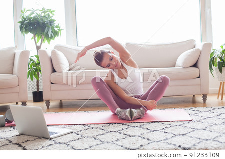 Cheerful woman doing fitness stretching exercises and using laptop at home. Cheerful woman doing fitness stretching exercises and using laptop at home. 91233109