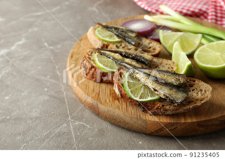 Board with sandwiches with sprats on gray textured background Board with sandwiches with sprats on gray textured background 91235405