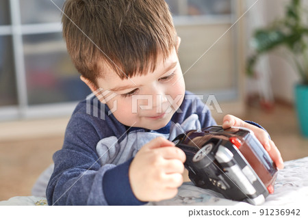 Indoor shot of good looking small kid holds toy car in hands, poses indoor against cozy domestic interior, likes to play with toys, has appealing look. Joyful cute boy preschooler being naughty Indoor shot of good looking small kid holds toy car in hands, poses indoor against cozy domestic interior, likes to play with toys, has appealing look. Joyful cute boy preschooler being naughty 91236942
