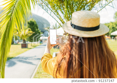 Trendy woman with brown hair wears straw hat using phone outdoors. White blank empty screen display. Connection, technology, apps, mock up, web site, copy space, communication concept. No face Trendy woman with brown hair wears straw hat using phone outdoors. White blank empty screen display. Connection, technology, apps, mock up, web site, copy space, communication concept. No face 91237147