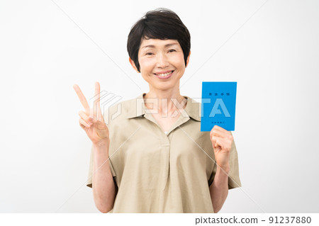 A middle-aged woman holding a pension book and signing a peace sign 91237880