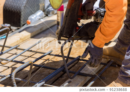 Using a rebar tying tool, construction worker twists steel bars with wire rods Using a rebar tying tool, construction worker twists steel bars with wire rods 91238688