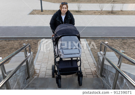 frustrated woman trying to climb stairs with baby stroller in her hands 91239071