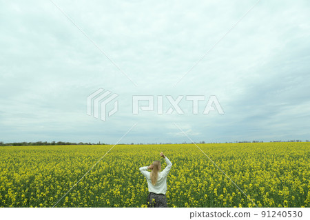 A girl stands in a rapeseed field on a summer day 91240530
