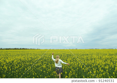 A girl stands in a rapeseed field on a summer day A girl stands in a rapeseed field on a summer day 91240531