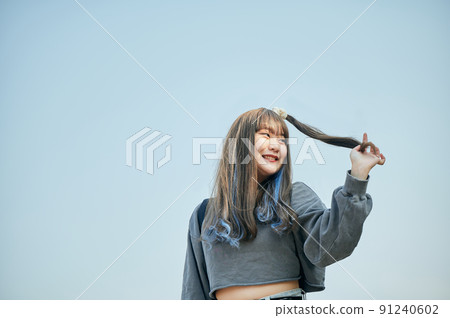 Gen Z woman standing against the blue sky 91240602