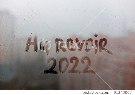 lettering Au revoir in French is goodbye in english and numbers 2022 paint with finger of water on splashed by rain foggy glass on sunset window lettering Au revoir in French is goodbye in english and numbers 2022 paint with finger of water on splashed by rain foggy glass on sunset window 91243063