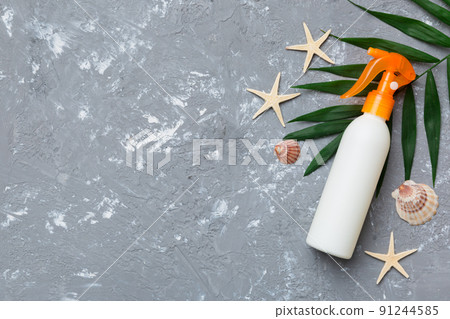 Sunscreen spray bottle. Bottle with sun protection cream and sea shells with tropical green leaf on color background, top view 91244585