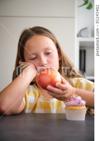 the girl chooses between a cupcake and an apple 91245902