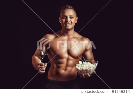 Strong, healthy man posing on a black background. Bodybuilder, athlete eats cottage cheese . The concept of a healthy diet and a healthy lifestyle 91246214