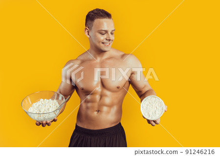 Strong, healthy man posing on a black background. Bodybuilder, athlete hold cottage cheese . The concept of a healthy diet and a healthy lifestyle 91246216