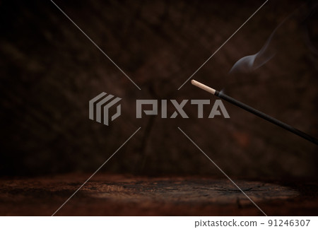 Lit incense on rustic dark wood background. Spiritual atmosphere, space for text. 91246307