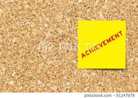 Yellow note paper with word achievement on cork board background with copy space 91247079