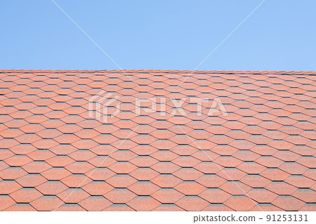 New roof with red shingles against the blue sky. High quality photo. Tiles on the roof of the house. Use to advertise roof fabrication and maintenance. Spotted texture. Affordable roofing. 91253131