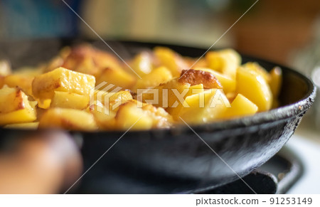 Roasting fresh potatoes in a cast iron skillet with sunflower oil. A view of a stovetop with a frying pan filled with golden fried potatoes in a real kitchen. Food cooked in a homemade frying pan. Roasting fresh potatoes in a cast iron skillet with sunflower oil. A view of a stovetop with a frying pan filled with golden fried potatoes in a real kitchen. Food cooked in a homemade frying pan. 91253149
