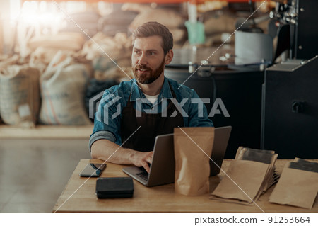 Business owner of small coffee factory working laptop on background of coffee roast machine 91253664