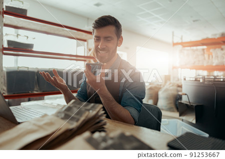 Male barista record audio message on phone working on small coffee factory Male barista record audio message on phone working on small coffee factory 91253667
