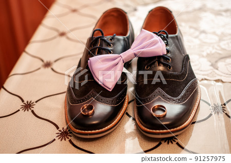 Pair of gold wedding rings and pink bowtie on the black shoes 91257975