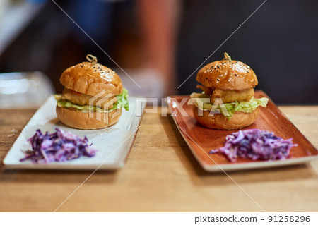 Tasty grilled beef burger with lettuce, ketchup, onion rings, chili and mayonnaise served on pieces of brown paper on a rustic wooden table of counter. 91258296