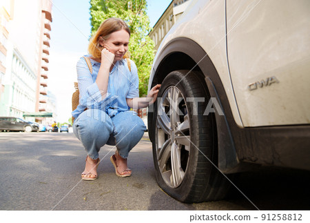 a sad woman sits at the punctured wheel of a car. tire service. solar glare a sad woman sits at the punctured wheel of a car. tire service. solar glare 91258812