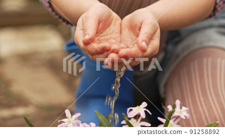 a little girl watering flowers from the palms of her hands. 91258892