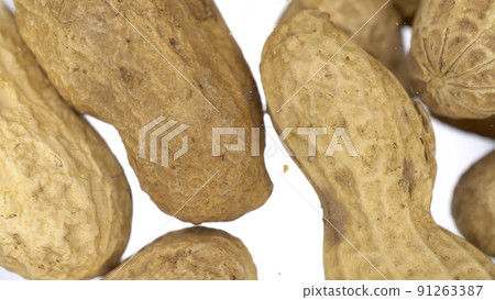 Peanuts in the skin falls on the glass on a bright white background. Peanut close up view from below. Peanuts in the skin falls on the glass on a bright white background. Peanut close up view from below. 91263387