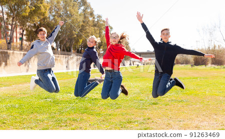 Friendly teenagers jumping together in park Friendly teenagers jumping together in park 91263469