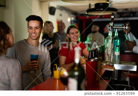 Young people with cocktails in hands chatting near the bar in nightclub Young people with cocktails in hands chatting near the bar in nightclub 91263599