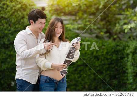 happy pregnant woman with husband watching ultrasound photo of baby. married couple. 91265785
