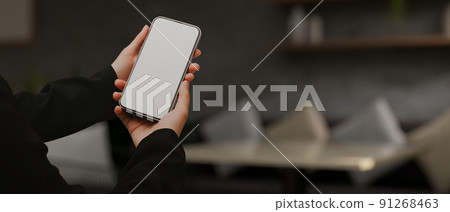 A female hands holding a mobile phone white screen mockup over blurred modern living room A female hands holding a mobile phone white screen mockup over blurred modern living room 91268463