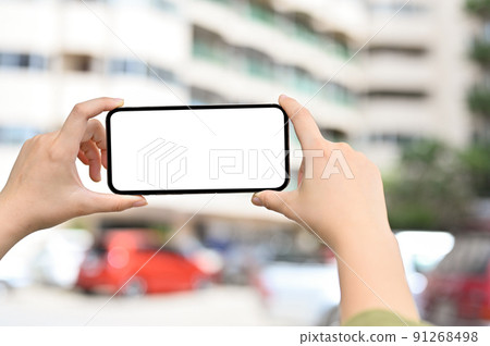 Close-up, A female hands holding a smartphone over blurred apartment building 91268498