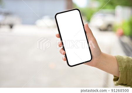 A female hand holding a smartphone mockup over blurred road or street in the background. 91268500