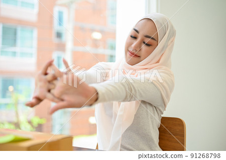 Relaxed young asian muslim businesswoman wearing hijab stretching her arms, feeling tired 91268798