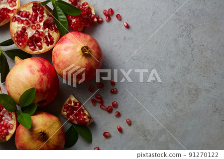 Ripe pomegranate fruit and half, seeds pomegranate with leaves on grey concrete background. Vegan, healthy diet concept. Top view, horizontal, with copy space. Ripe pomegranate fruit and half, seeds pomegranate with leaves on grey concrete background. Vegan, healthy diet concept. Top view, horizontal, with copy space. 91270122