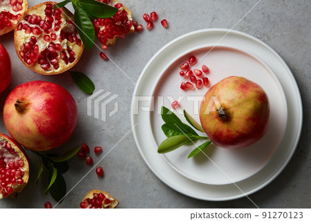 Ripe pomegranate fruit and half, seeds pomegranate with leaves on grey concrete background. Fresh pomegranate on white plate. Vegan, healthy diet concept. Top view. Ripe pomegranate fruit and half, seeds pomegranate with leaves on grey concrete background. Fresh pomegranate on white plate. Vegan, healthy diet concept. Top view. 91270123