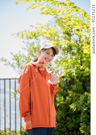 A young and cute woman walking with a plastic bottle for hydration in the sunny sunshine A young and cute woman walking with a plastic bottle for hydration in the sunny sunshine 91275211
