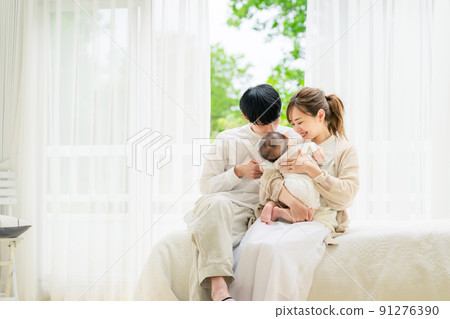 Family image of a couple holding a baby relaxing in the room 91276390