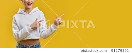 Unrecognizable girl indicating right direction with fingers indoors. Crop view of smiling female, pointing away with neat hands, isolated on yellow studio background, copy space. Concept of gesturing. 91279361