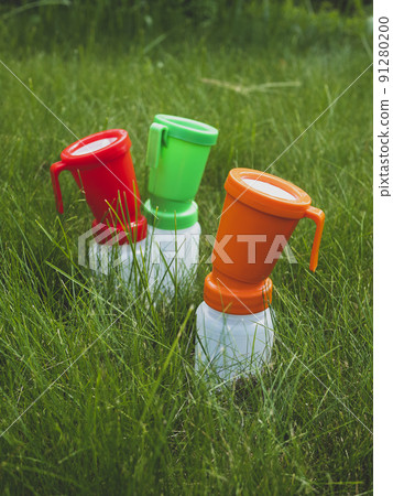 Three colored teat dip cups for cattle on the grass. Concept of hygiene and disinfection of cow's udder. Health care of udder before and after milking 91280200