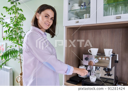 Young woman making coffee in coffee machine at home Young woman making coffee in coffee machine at home 91281424