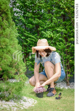 An Asian woman gardener is planting flowers into the flower pot. An Asian woman gardener is planting flowers into the flower pot. 91282418