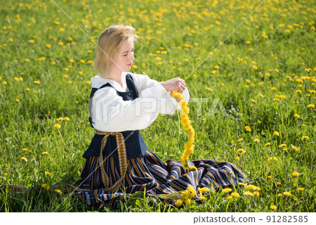 Young woman in national clothes wearing yellow dandelion wreath in spring field. Springtime 91282585