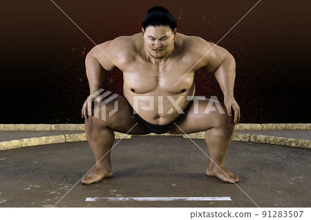A sumo wrestler with a rugged expression on the ring is stepping on his fork with a dignified aura. 91283507