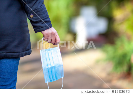 Woman, standing at the grave of family members with a facemask during the pandemic Woman, standing at the grave of family members with a facemask during the pandemic 91283673
