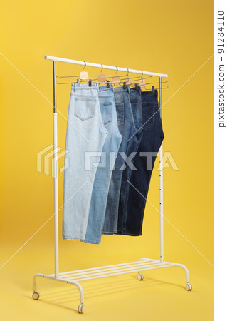 Rack with different jeans on yellow background Rack with different jeans on yellow background 91284110