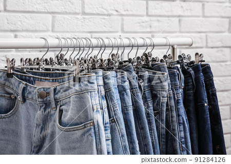 Rack with stylish jeans near brick wall, closeup 91284126
