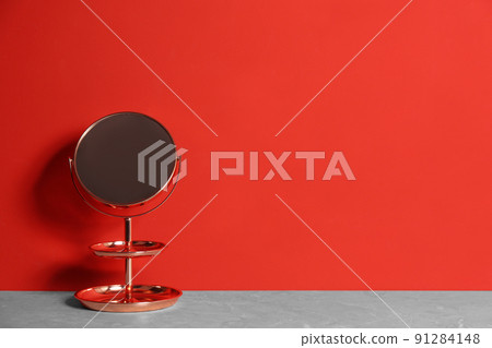 Small mirror on grey marble table near red wall. Space for text 91284148