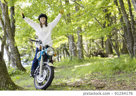 Bike girl image: A young woman standing on a motorcycle step in the forest and hurraying 91284176